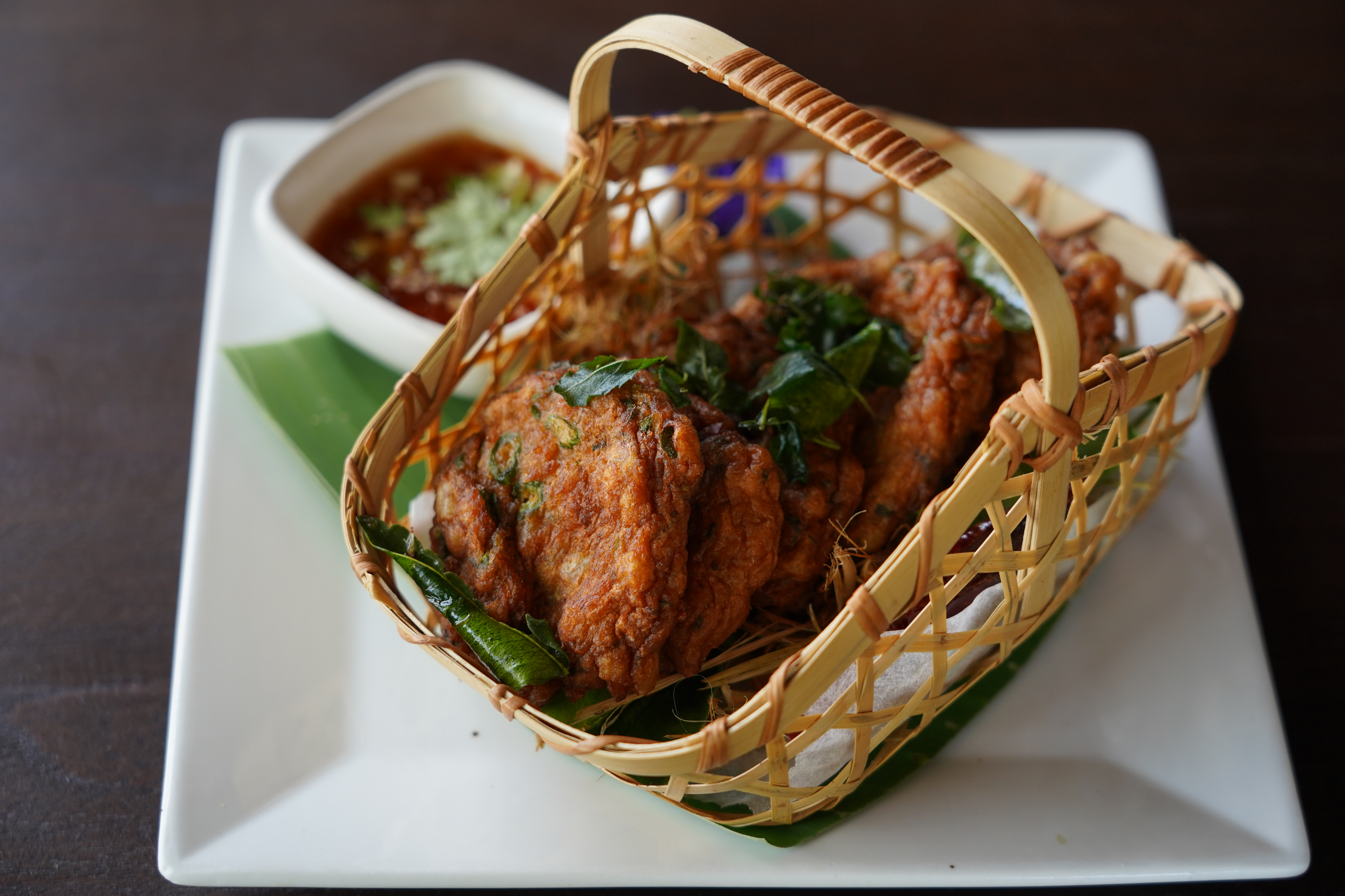Pla Hed — Sukhothai-style fish cakes in a handwoven bamboo basket on banana leaf with dipping sauce
