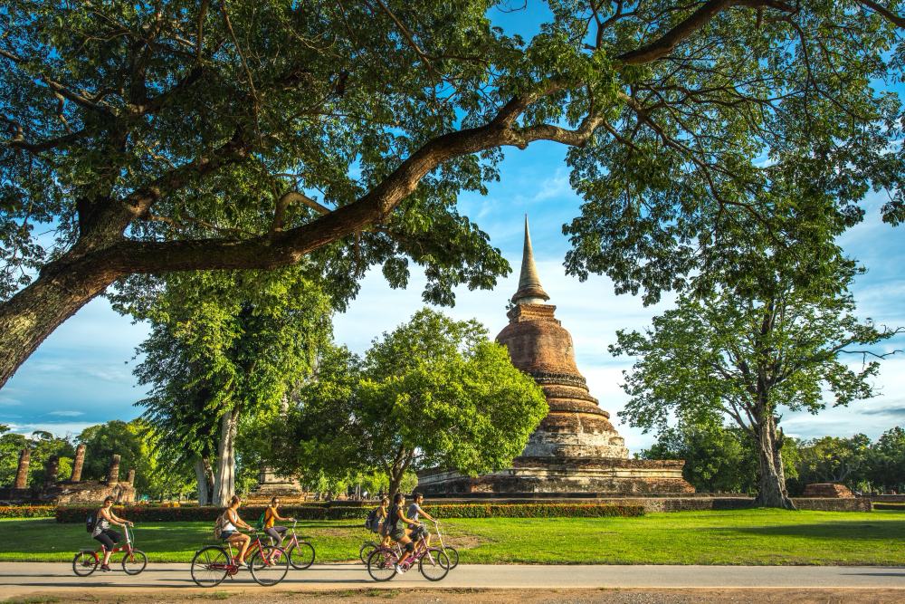นักปั่นจักรยานบนถนนสงบในชนบทสุโขทัย — ทุ่งนาและซากวัดอยู่เบื้องหลัง
