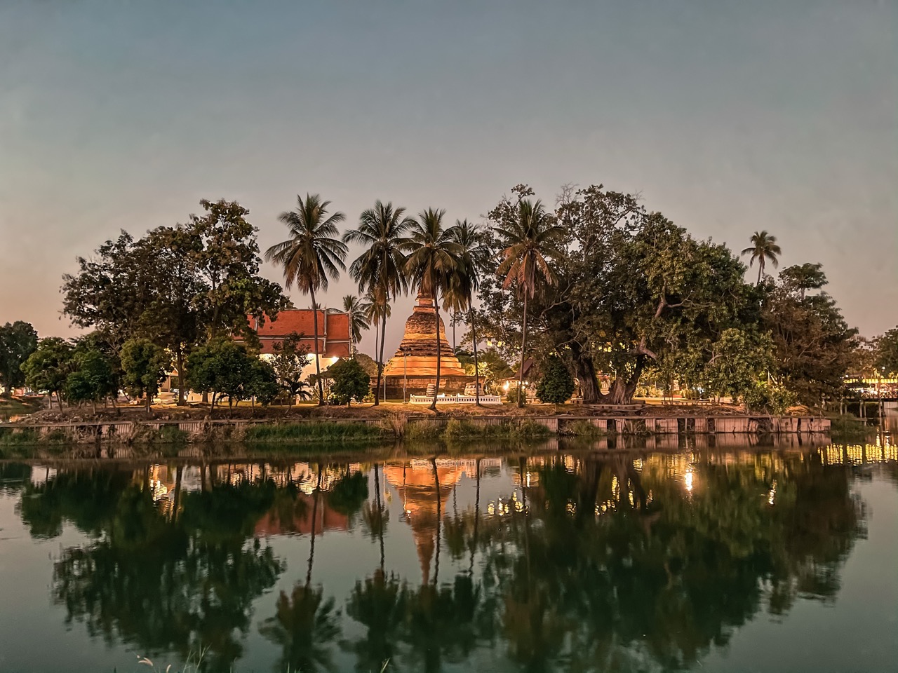 Stone prang of the Sukhothai Historical Park at sunrise, reflected in the lotus moat