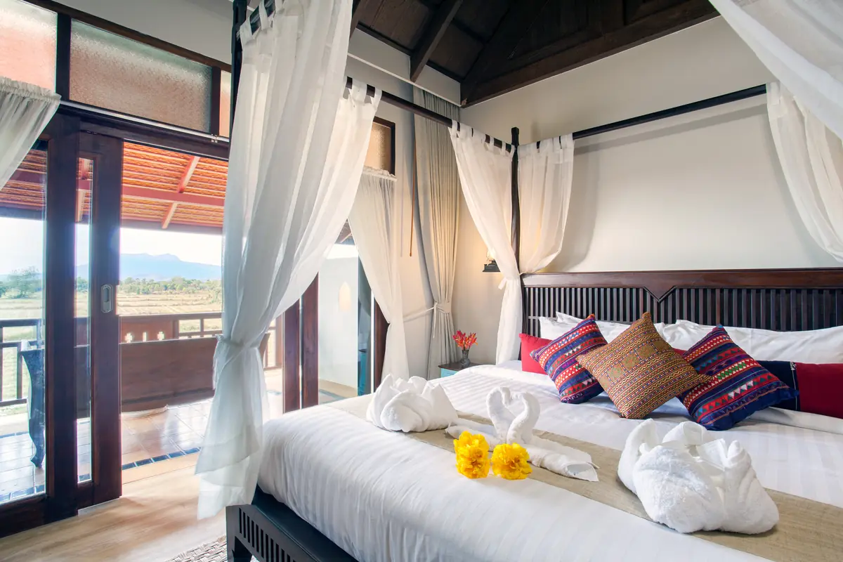 Deluxe Room — four-poster bed with open balcony doors and mountain view at golden hour